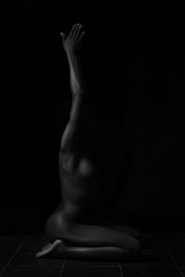 Black-and-white side profile of a person seated in a kneeling yoga pose with arms reaching overhead, illustrating the sacred practice of sensual yoga, presence, and embodied movement.